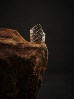 Adjustable, textured 925 silver sculpture ring resting on a rock. 