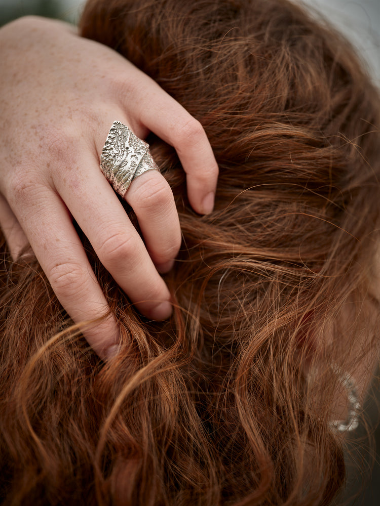 A hand in the hair wearing a textured silver ring.