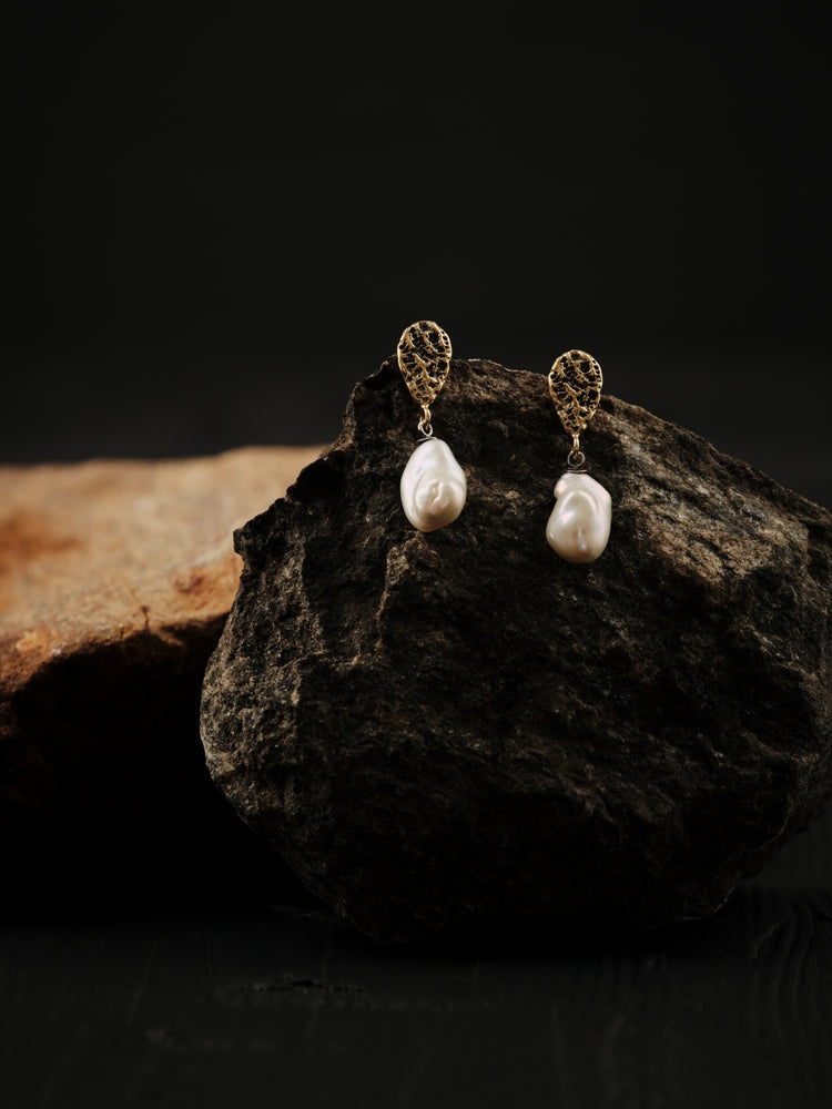 Earrings formed in two parts. The upper part is brass and teardrop-shaped, connected to the lower part which is a white keshi pearl.