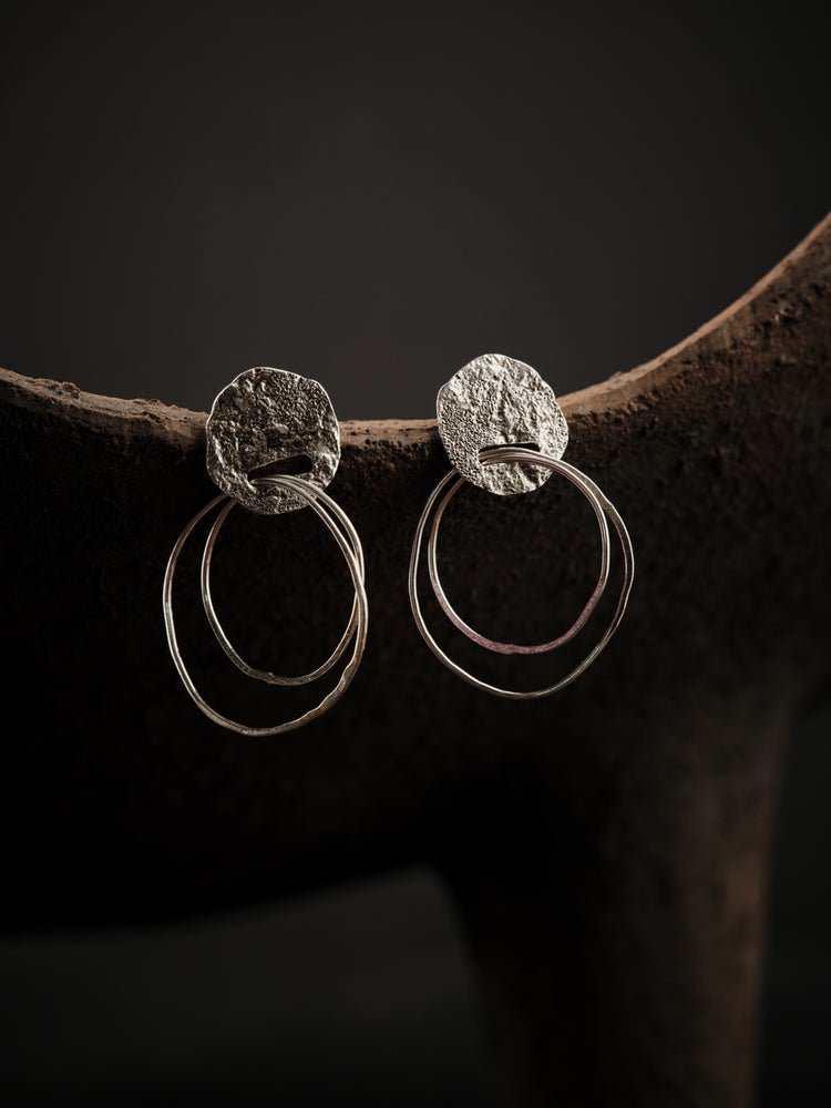 Silver earrings featuring a textured, openwork upper section into which two small silver hoops are inserted.