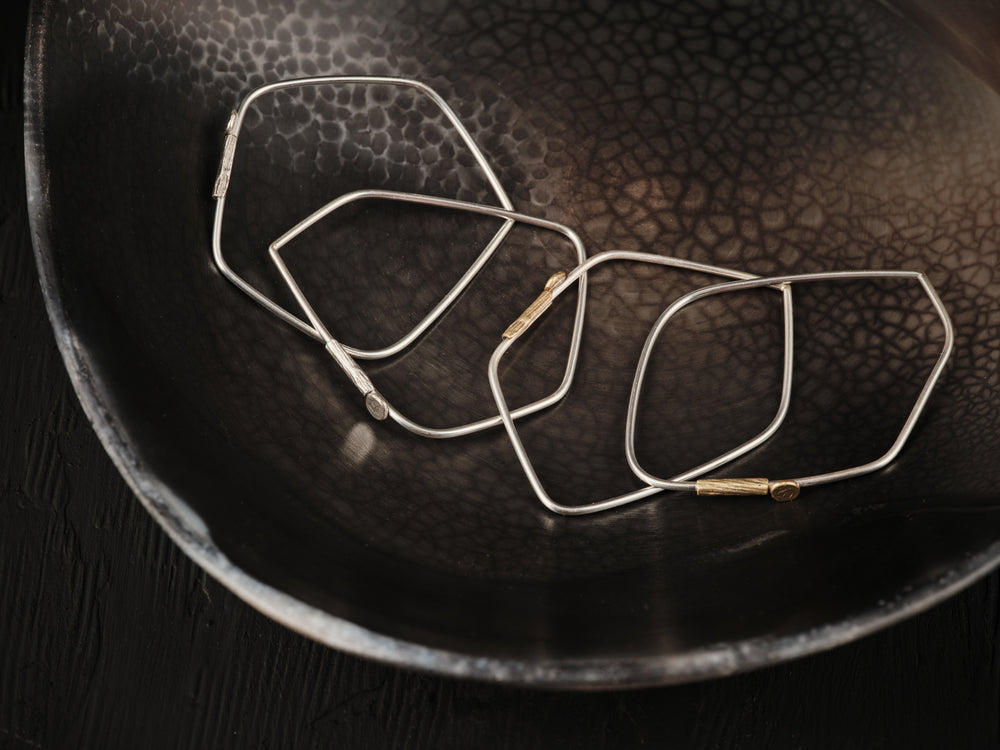 Four silver and brass bracelets are placed on a plate. Each bracelet has a different geometric shape.