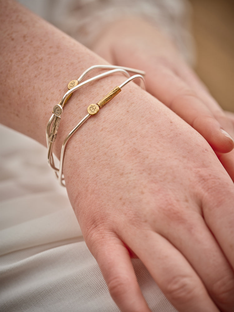 Close-up of a wrist wearing three silver and brass bracelets