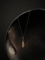 Long, geometric and textured pendant made of brass suspended from an oxidized silver chain.