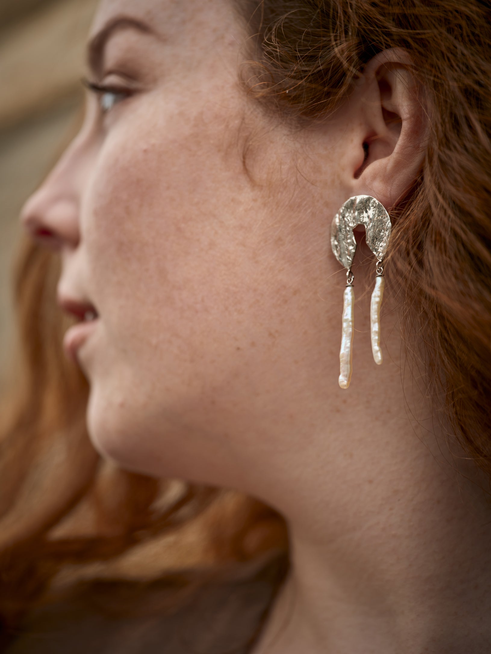 Profil d'une femme portant une boucles d'oreille en argent texturé et perle blanche