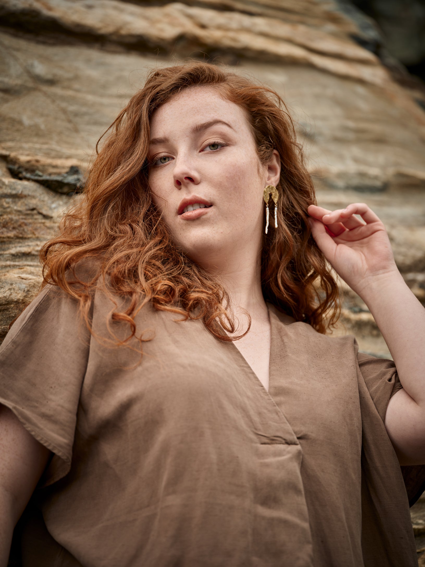 Femme adossée à un rocher portant une boucle d'oreille composé de laiton et de perle