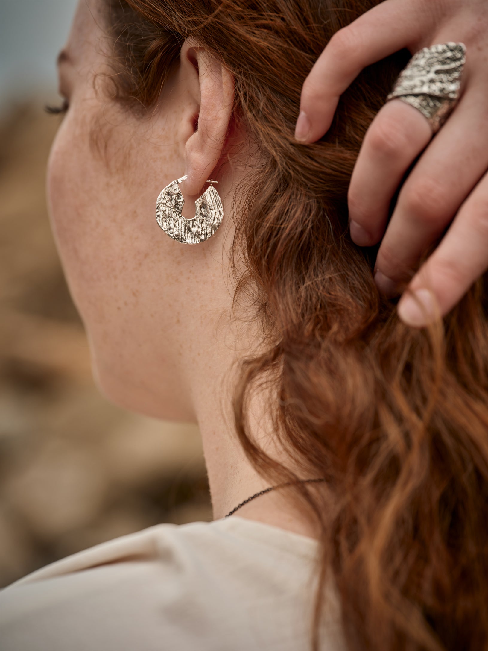 Femme la main dans les cheveux portant une bague et une boucles d'oreille en forme de disque de couleur argent