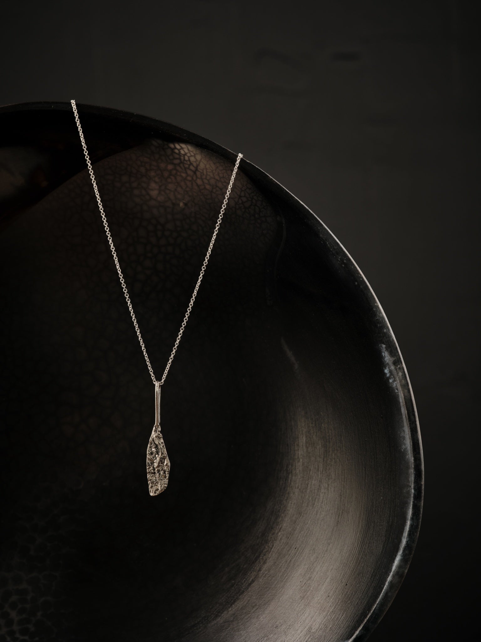 Pendentif longiforme, géométrique et texturé fabriqué en argent suspendu à une chaîne en argent.